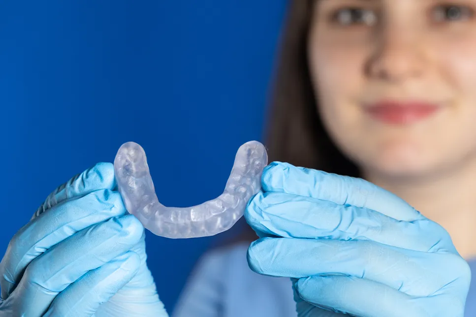 Asmuo su medicininėmis pirštinėmis laiko dantų kapą, skirtą sąkandžio ir žandikaulio sąnario (SAŽS) terapijai